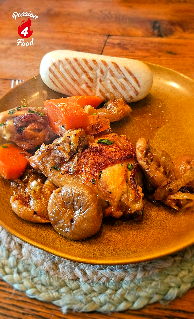 Een stoofgerecht met kip, groenten en tomatengarnituur, geserveerd op een houten tafel.
