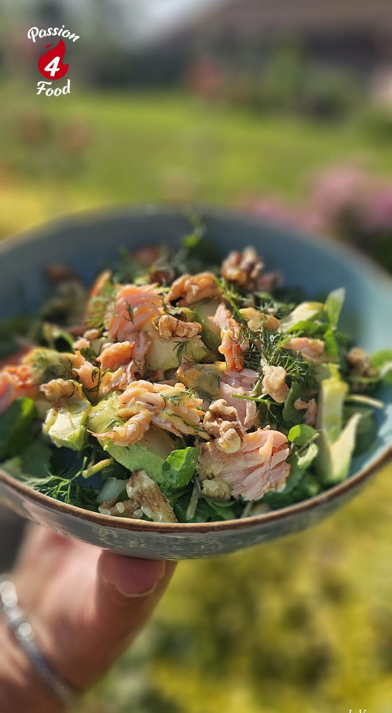 Handzame kom met gehakte salade met kruiden, bladgroenten en zalm, tegen een wazige tuinachtergrond.