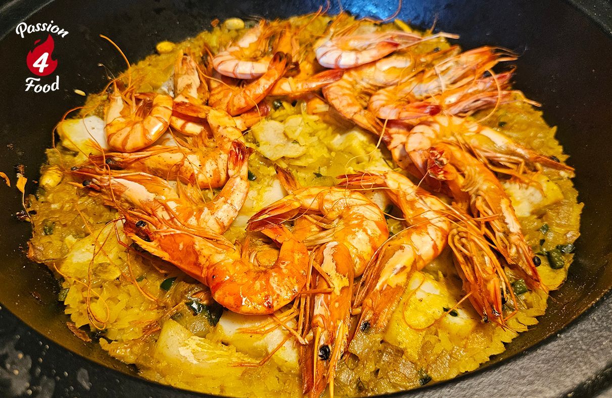 Seafood pilav in een zwarte pan, met vis, oranje garnalen over gele rijst en bouillon.
