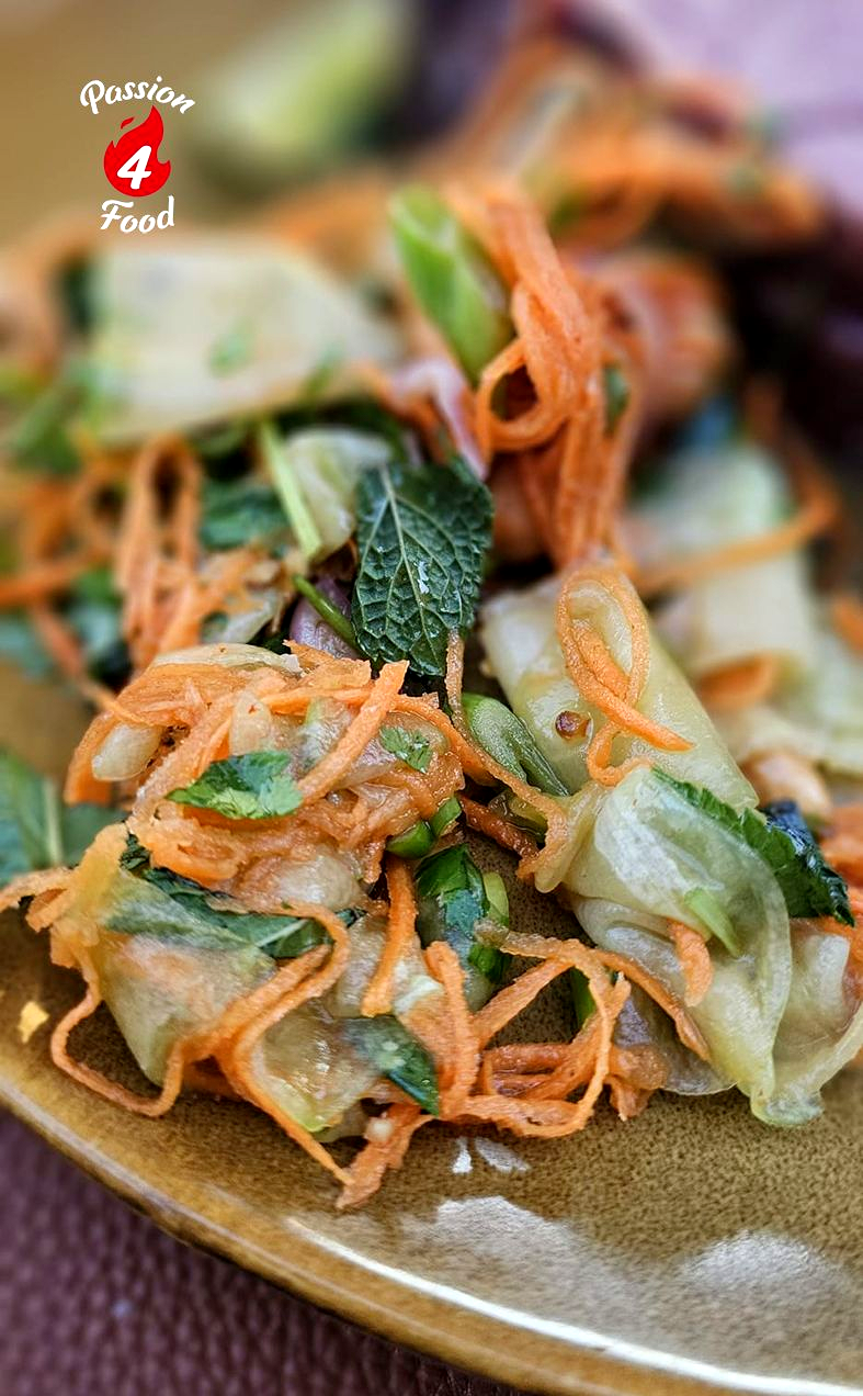 Knapperige gebakken noedels en een groentesalade met groene bladeren en geraspte wortelen op een bord.
