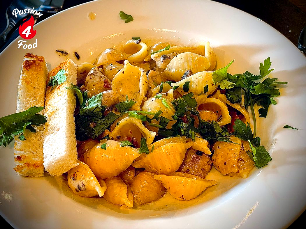 White bowl of seasoned conchiglie with herbs and mushroomsauce and garnished with parsley