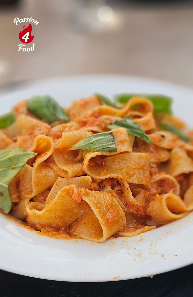 Een bord met oranje pasta, gegarneerd met groene kruiden, geserveerd op een wit bord.