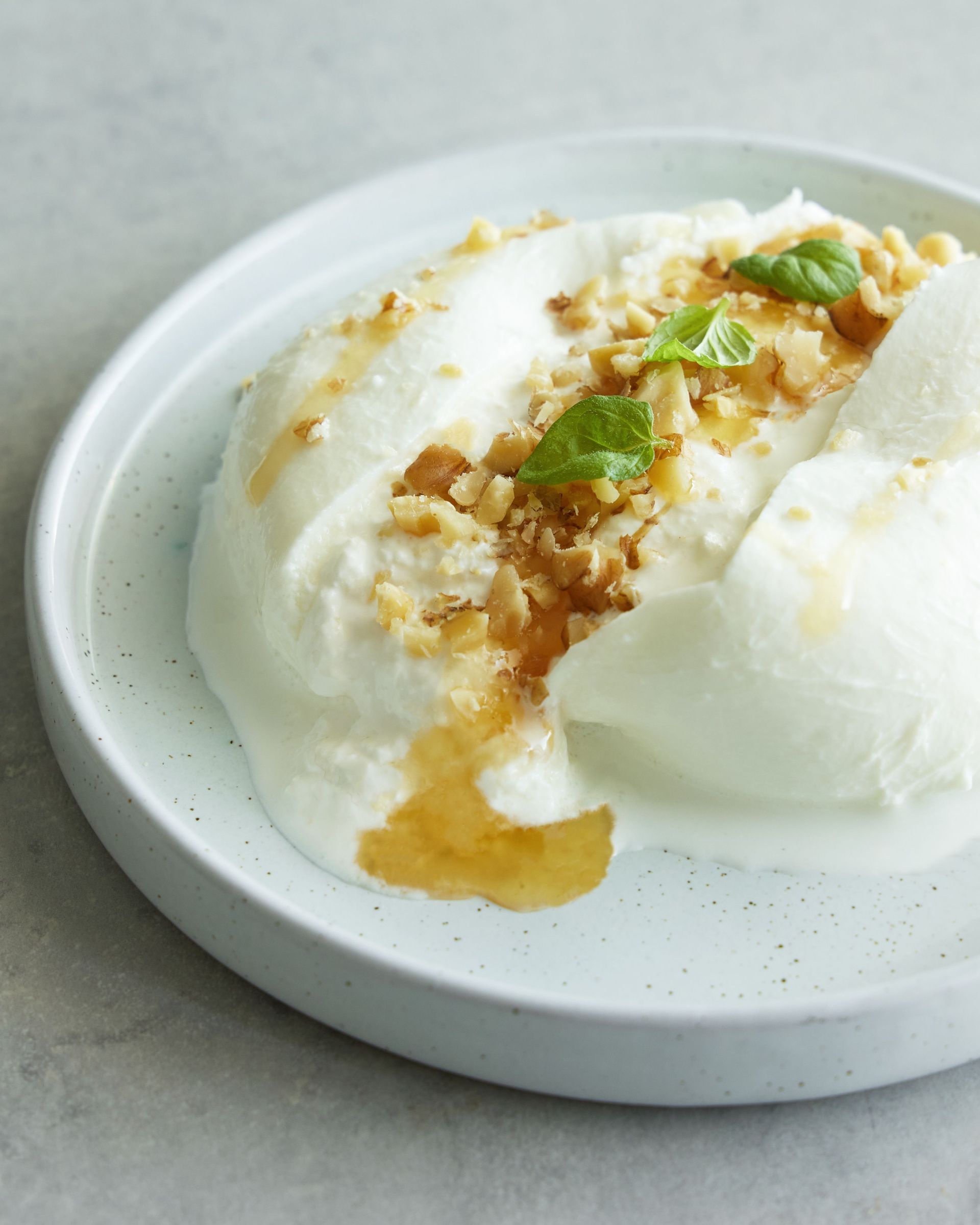 Burrata met olijfolie op wit bord met witte achtergrond.