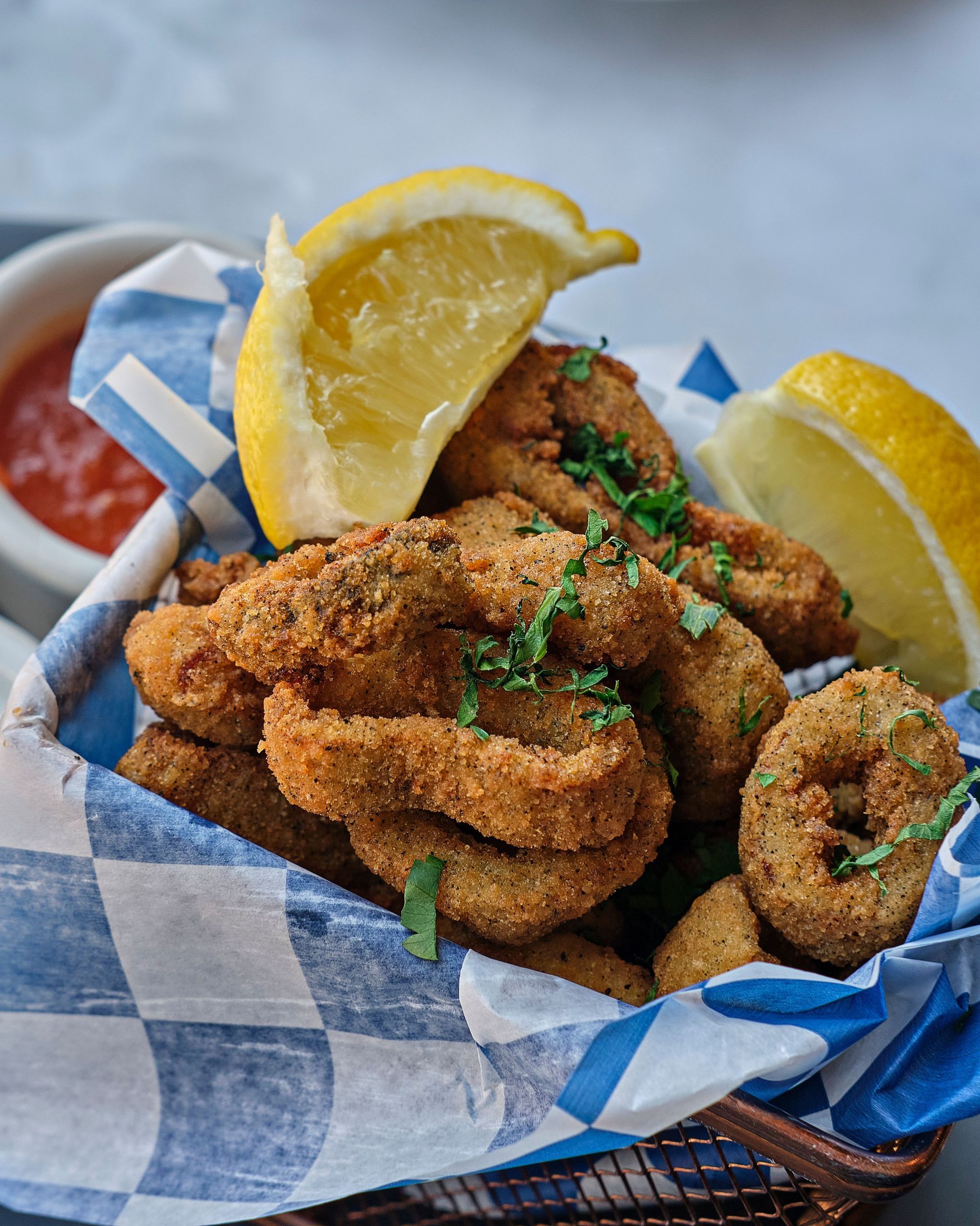 Basket of fried seafood with lemon wedges and parsley in blue checkered paper