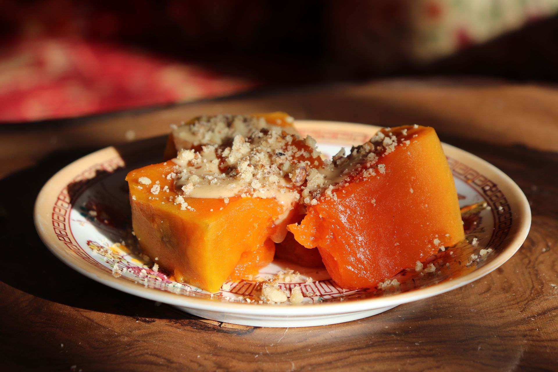 Oranje dessertblokjes met geraspte pistachenootjes erop, geserveerd op een bord.