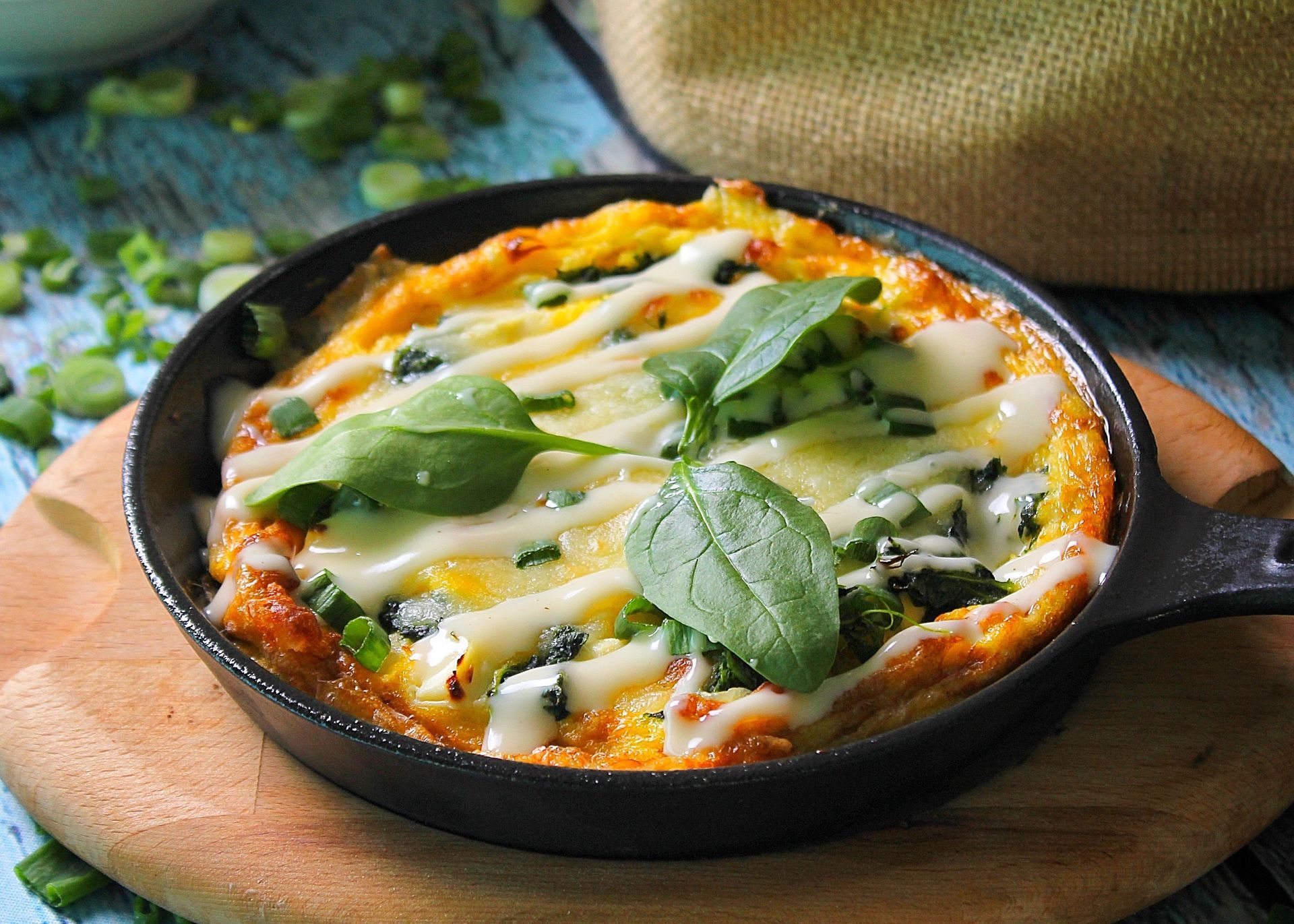 Een pan met gebakken frittata, gesmolten kaas en basilicum, geserveerd op een houten plank.