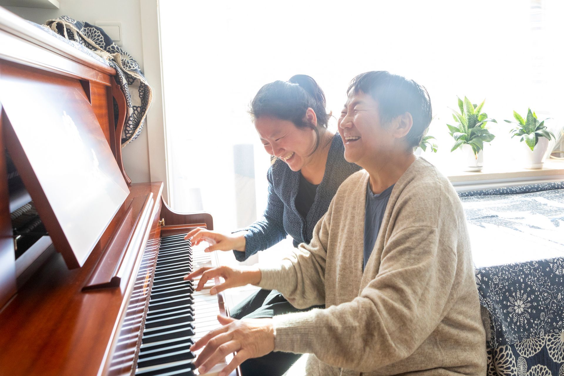 Two people smiling as they play a piano together in a bright room