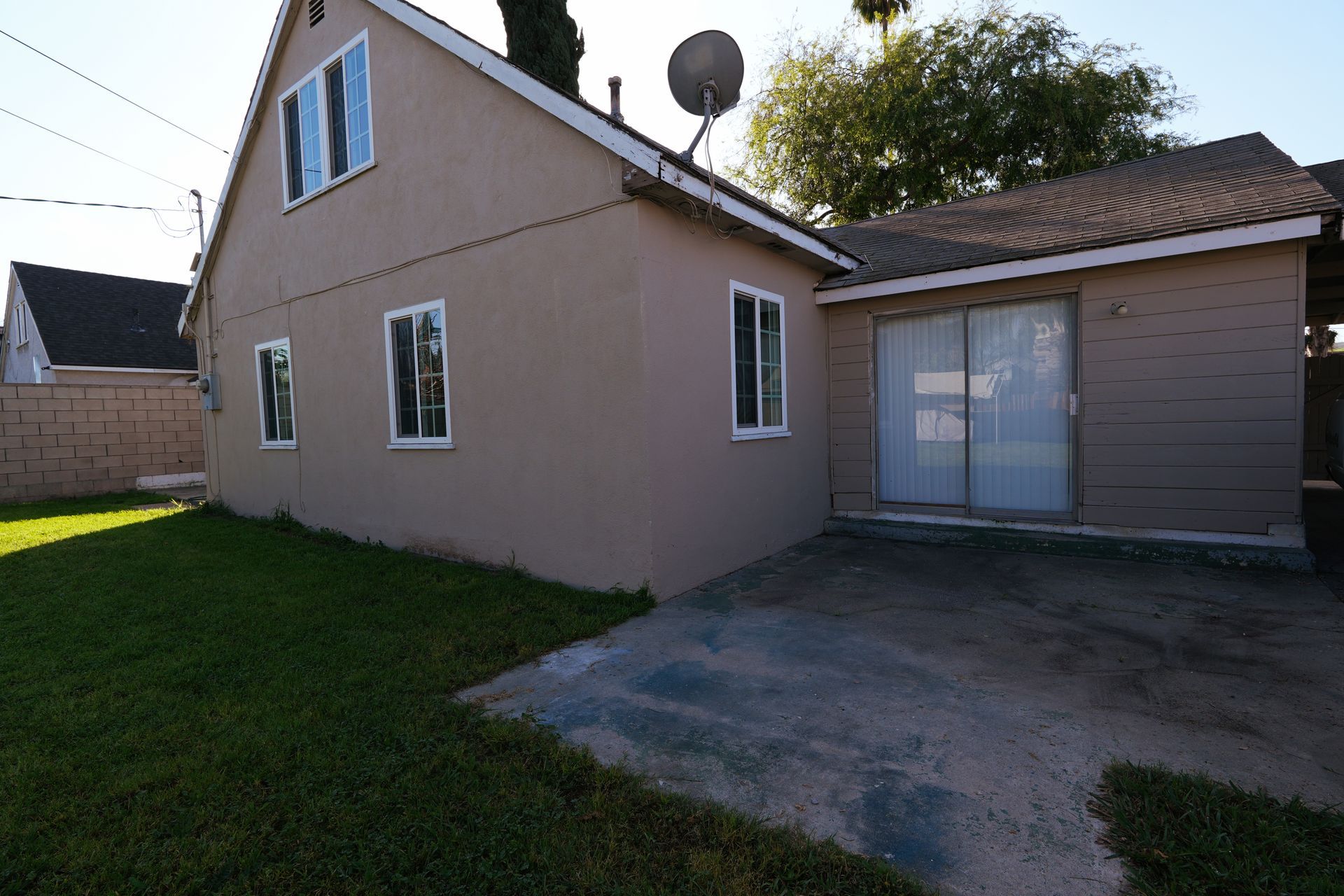 West Covina Suburban house exterior with beige siding, lawn, and a concrete driveway by sliding glass doors