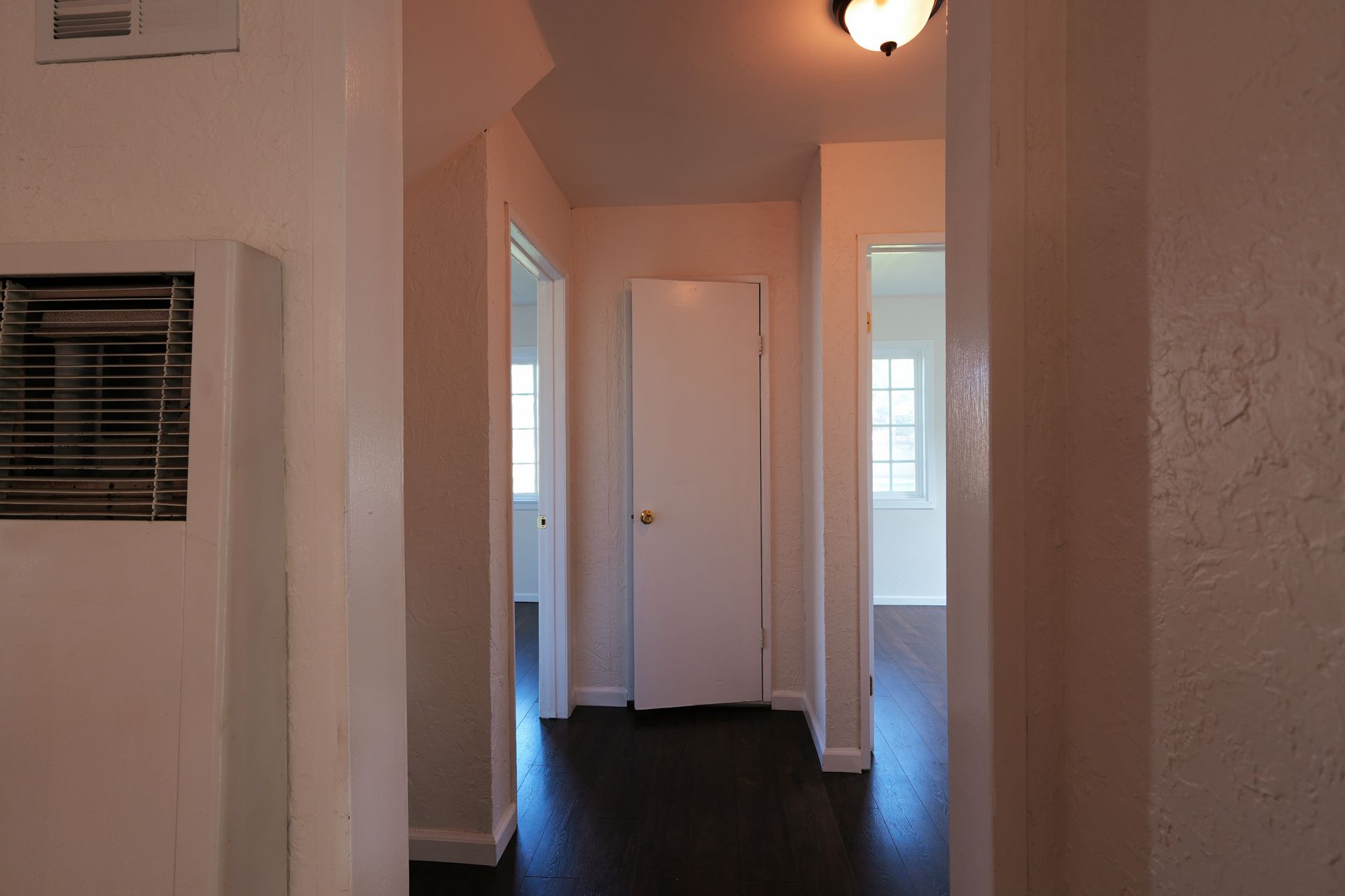 West Covina Narrow hallway with white walls, dark floor, and closed doors leading to a bright room.