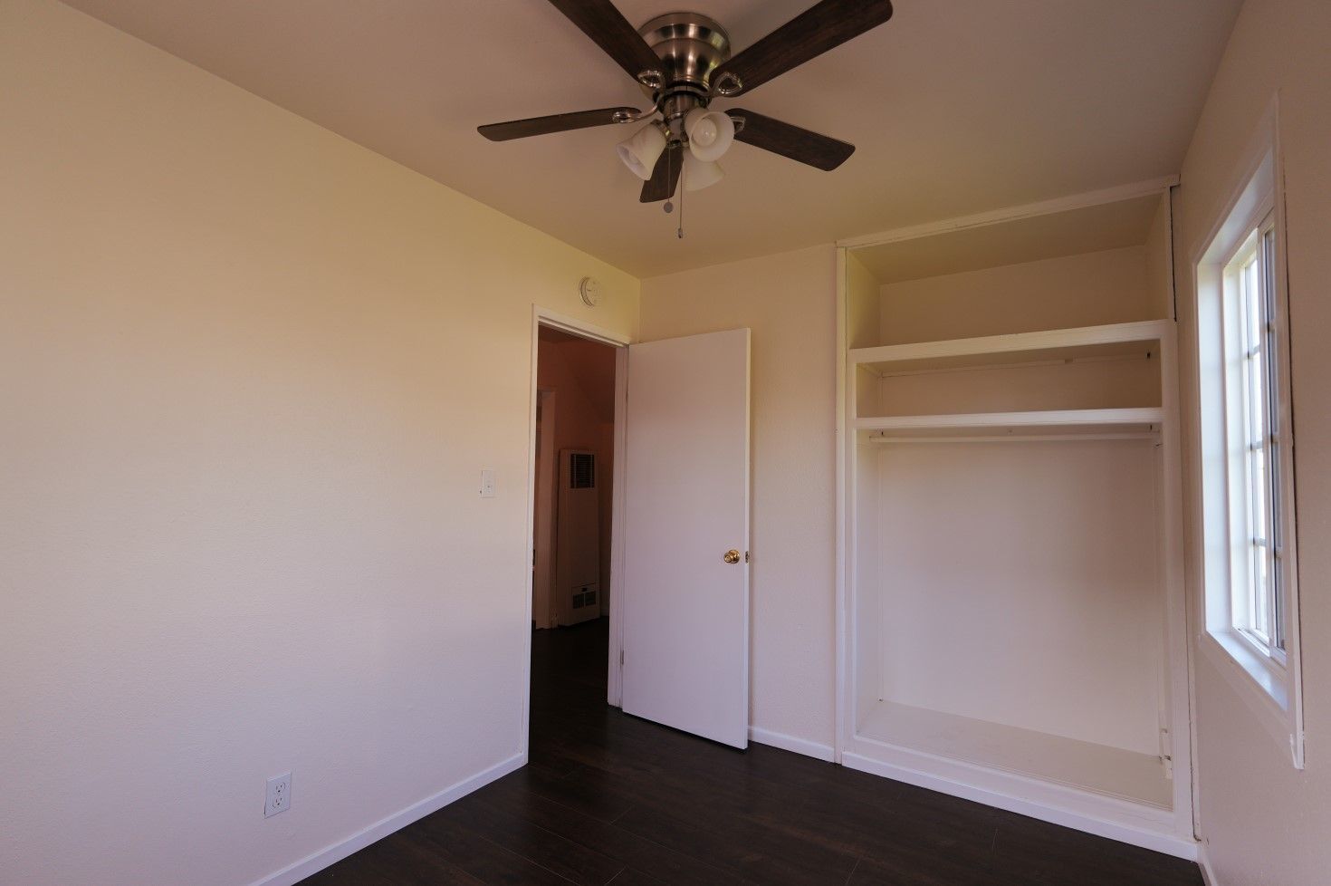 West Covina Empty beige bedroom with dark wood floor, ceiling fan, open closet, and window letting in light