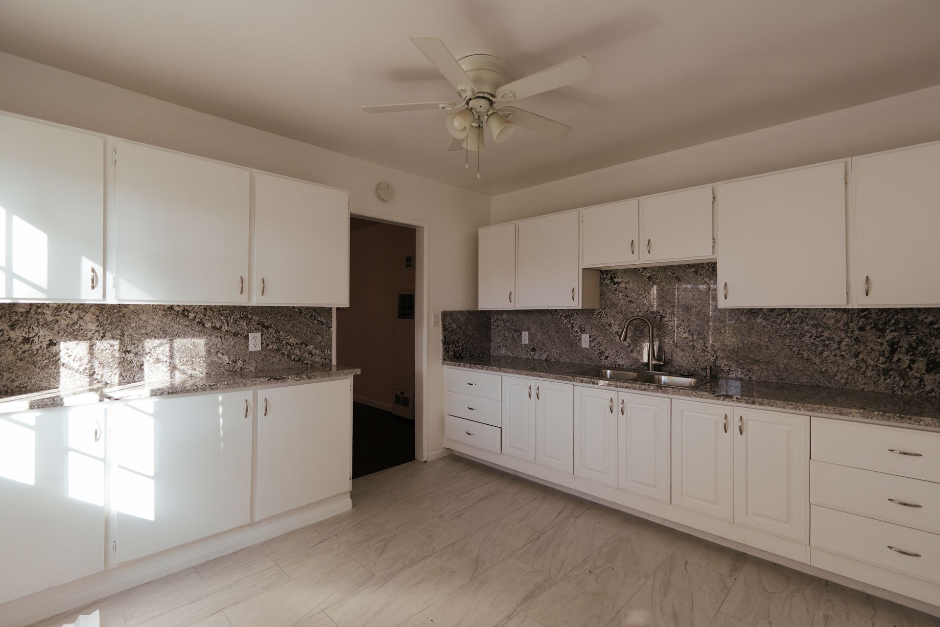 West Covina Bright kitchen with white cabinets, mosaic backsplash, beige tile floor, and ceiling fan.