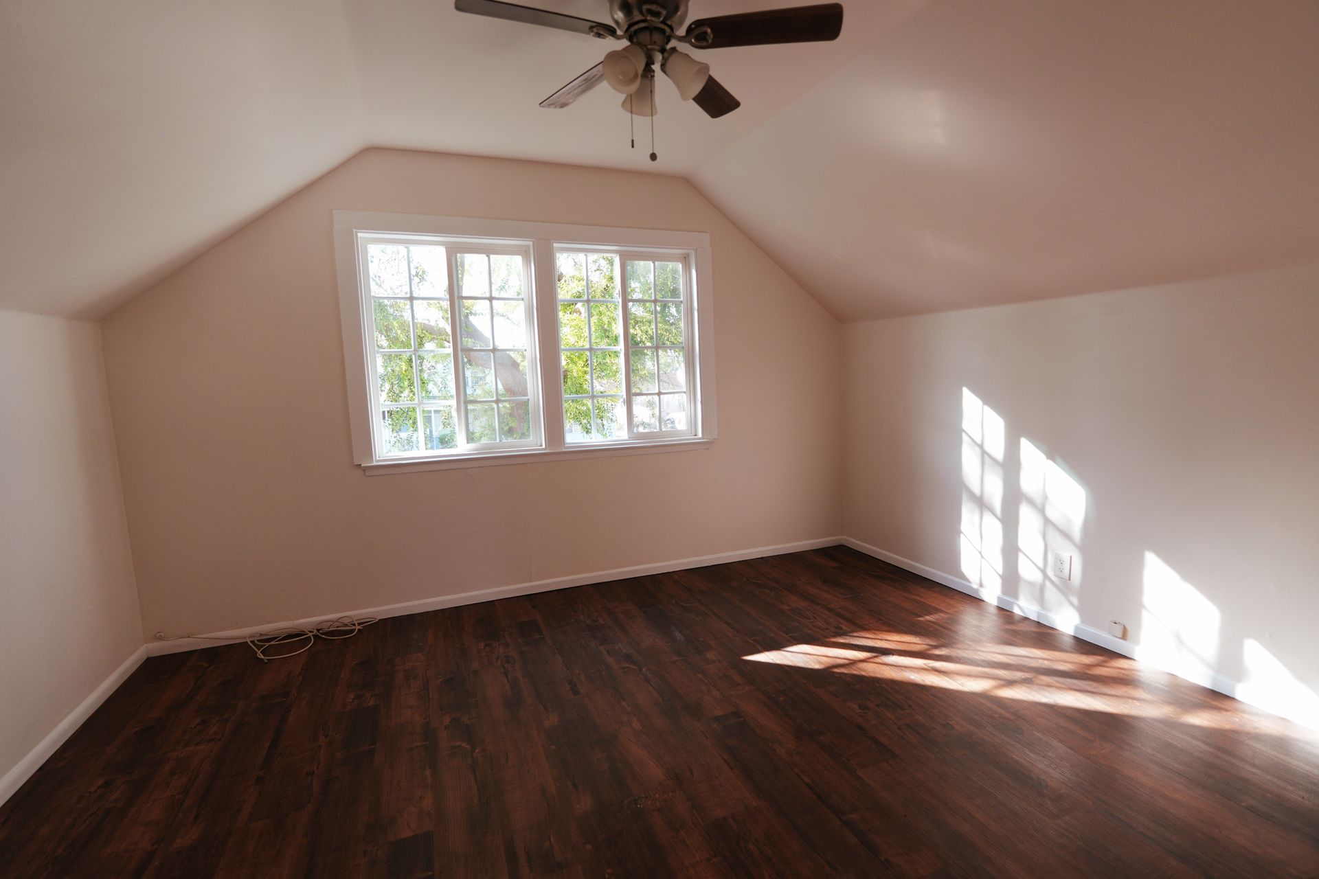 West Covina Empty attic room with dark wood floors, sloped ceiling, and sunlight through a window.