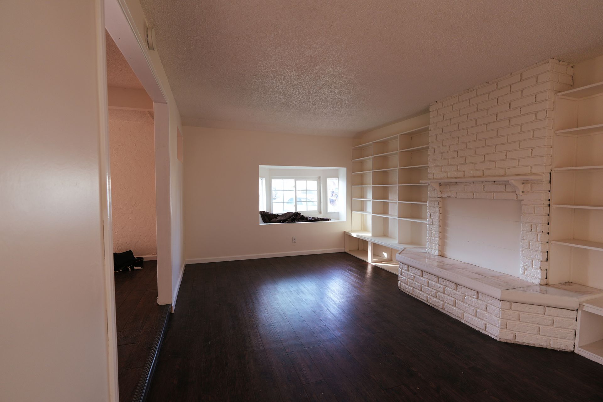 West Covina Empty living room with dark wood floor, white brick fireplace, and a window letting in daylight