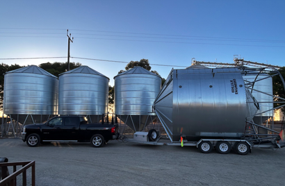 A combine harvester is loading grain into a silo next to a tractor.