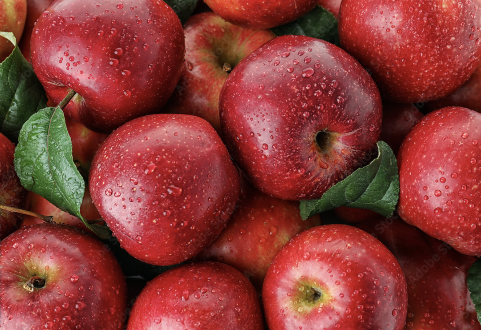 Un montón de manzanas rojas con hojas verdes sobre ellas.