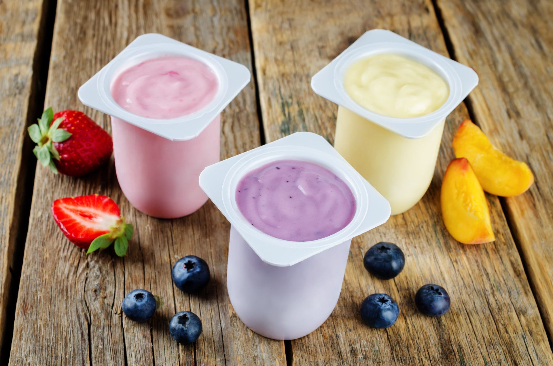 Sobre una mesa de madera hay tres sabores diferentes de yogur.