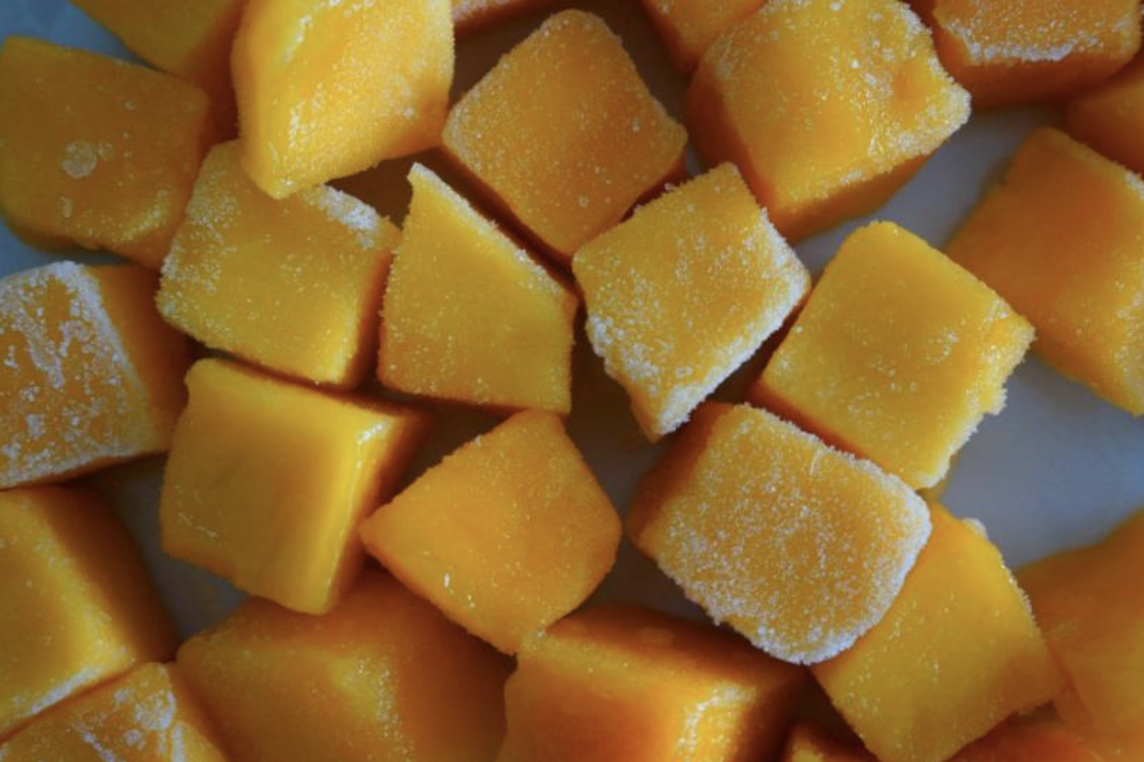 Una pila de cubos de mango congelados en un plato blanco.