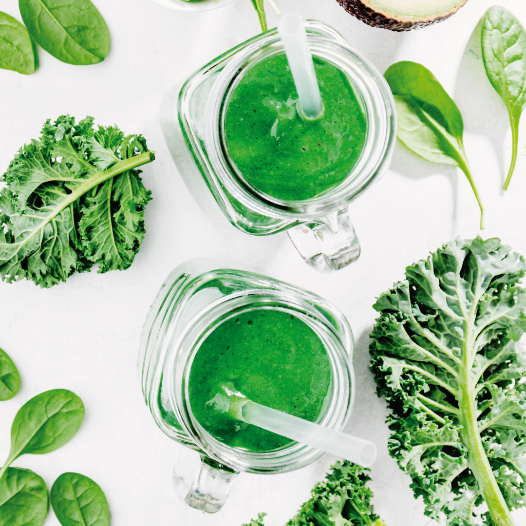 Dos batidos verdes con pajitas están rodeados de hojas verdes.