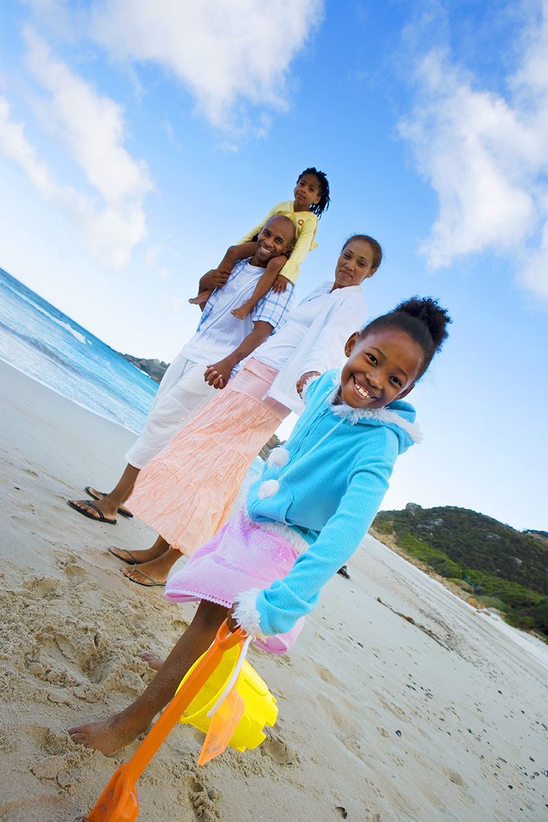 Three children play on a beach, one smiling in a blue hoodie holding a yellow scarf.