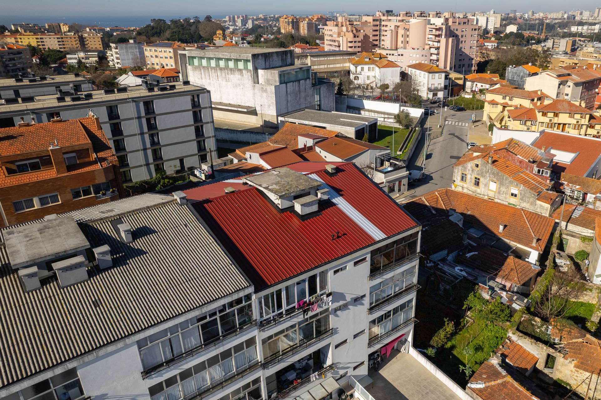 Vista aérea de uma cidade com edifícios. Telhados vermelhos e cinzentos, árvores verdes e um mar azul ao longe.