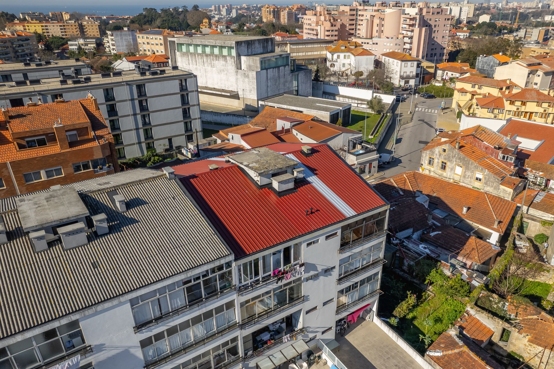 Vista aérea da paisagem urbana com diversos edifícios, telhados vermelhos e céu azul ao fundo.