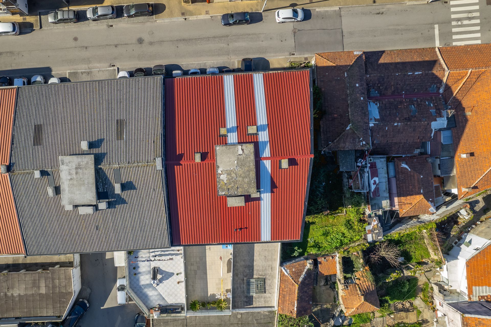 Vista aérea de telhados com telhas vermelhas, cinzas e laranjas. Carros estacionados em uma rua acima.