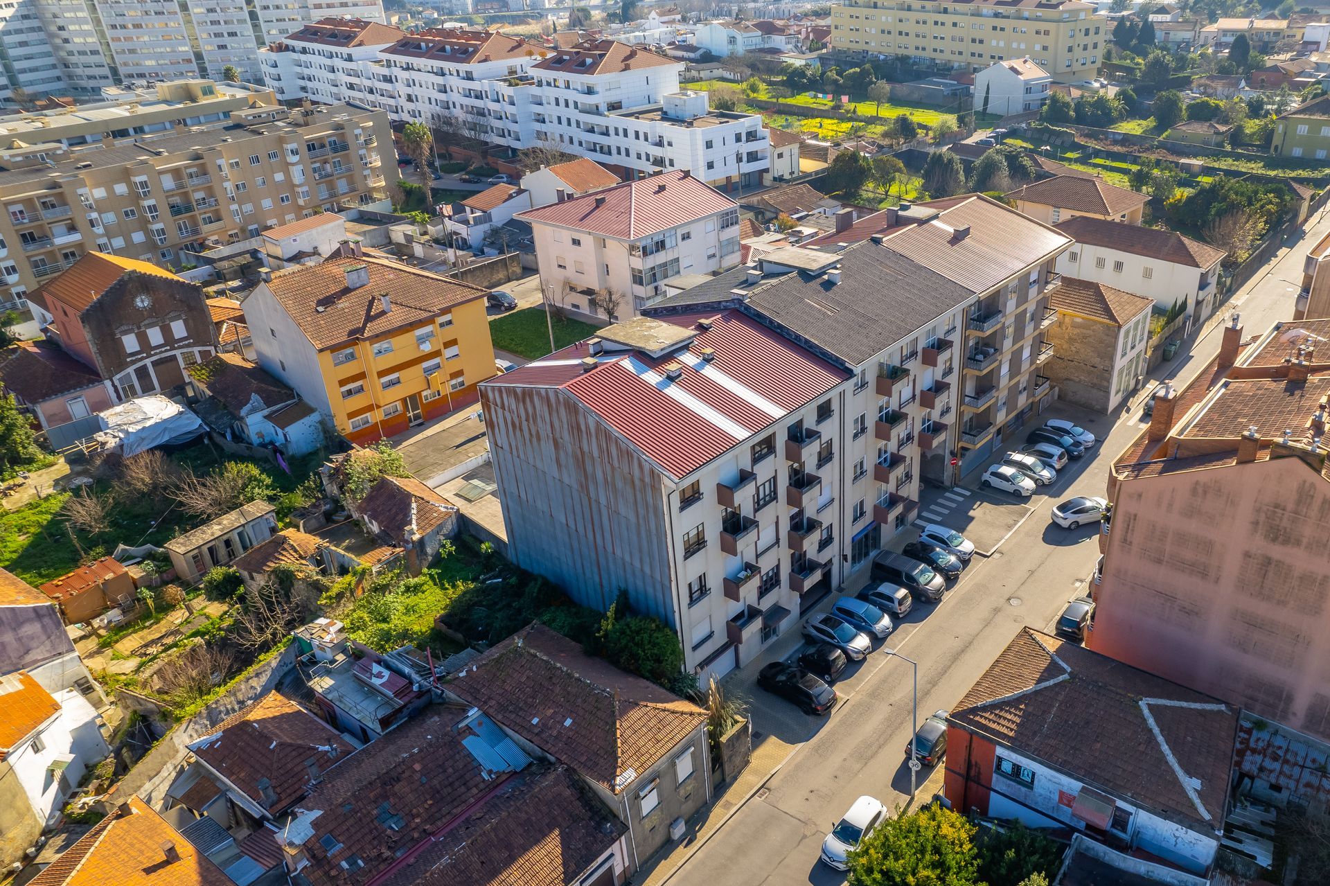 Vista aérea de edifícios com telhados de telha vermelha, carros estacionados ao longo de uma rua e áreas verdes.