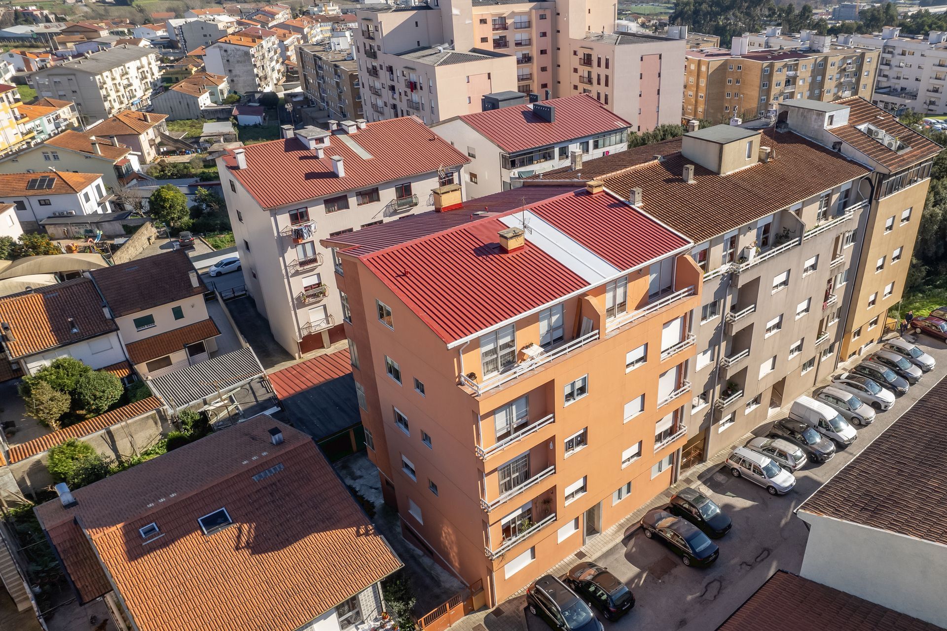 Vista aérea de prédios de apartamentos com telhados de telha laranja e vermelha e carros estacionados.