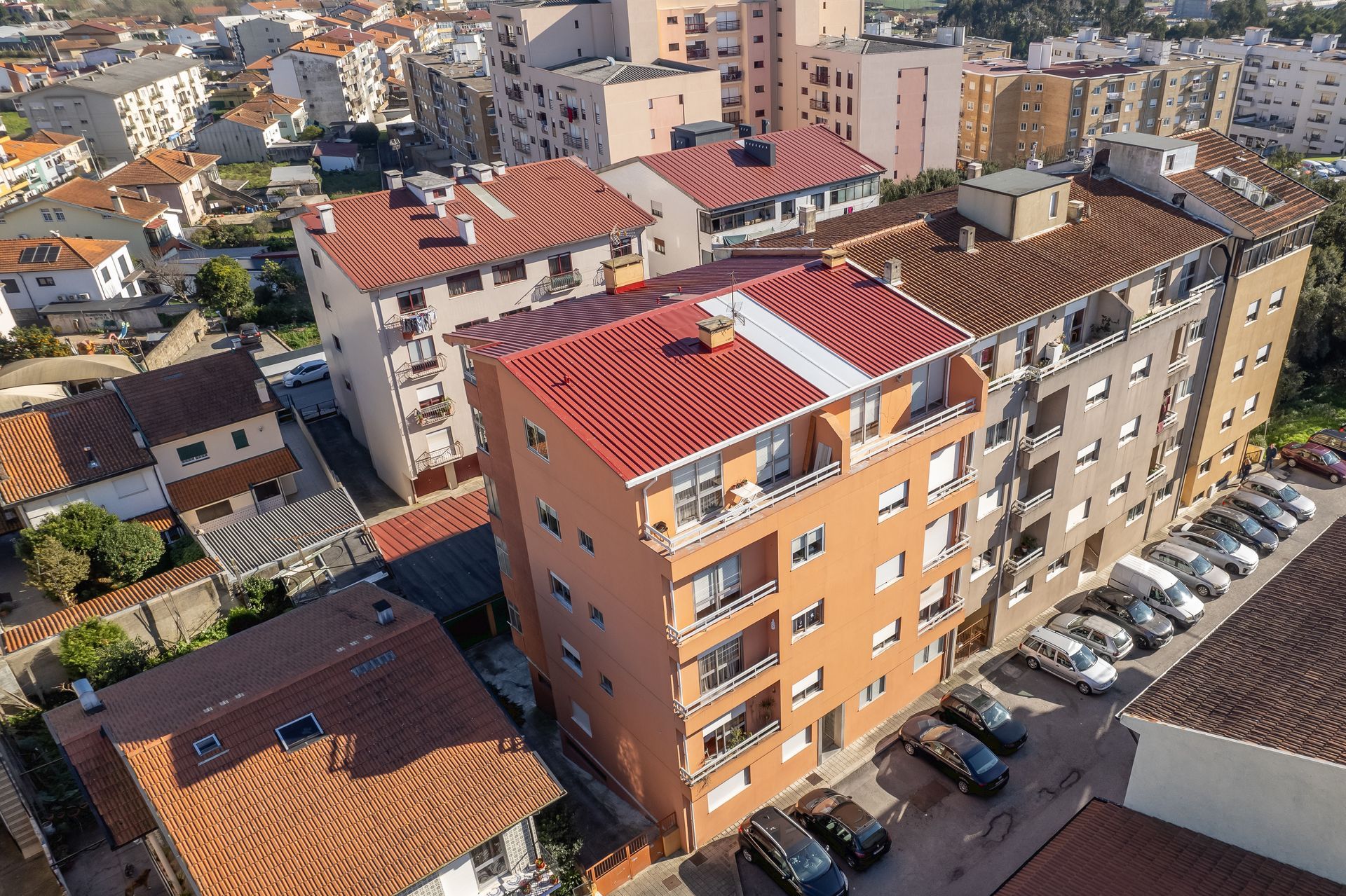 Vista aérea de prédios de apartamentos com telhados de telha vermelha e carros estacionados em um dia ensolarado.