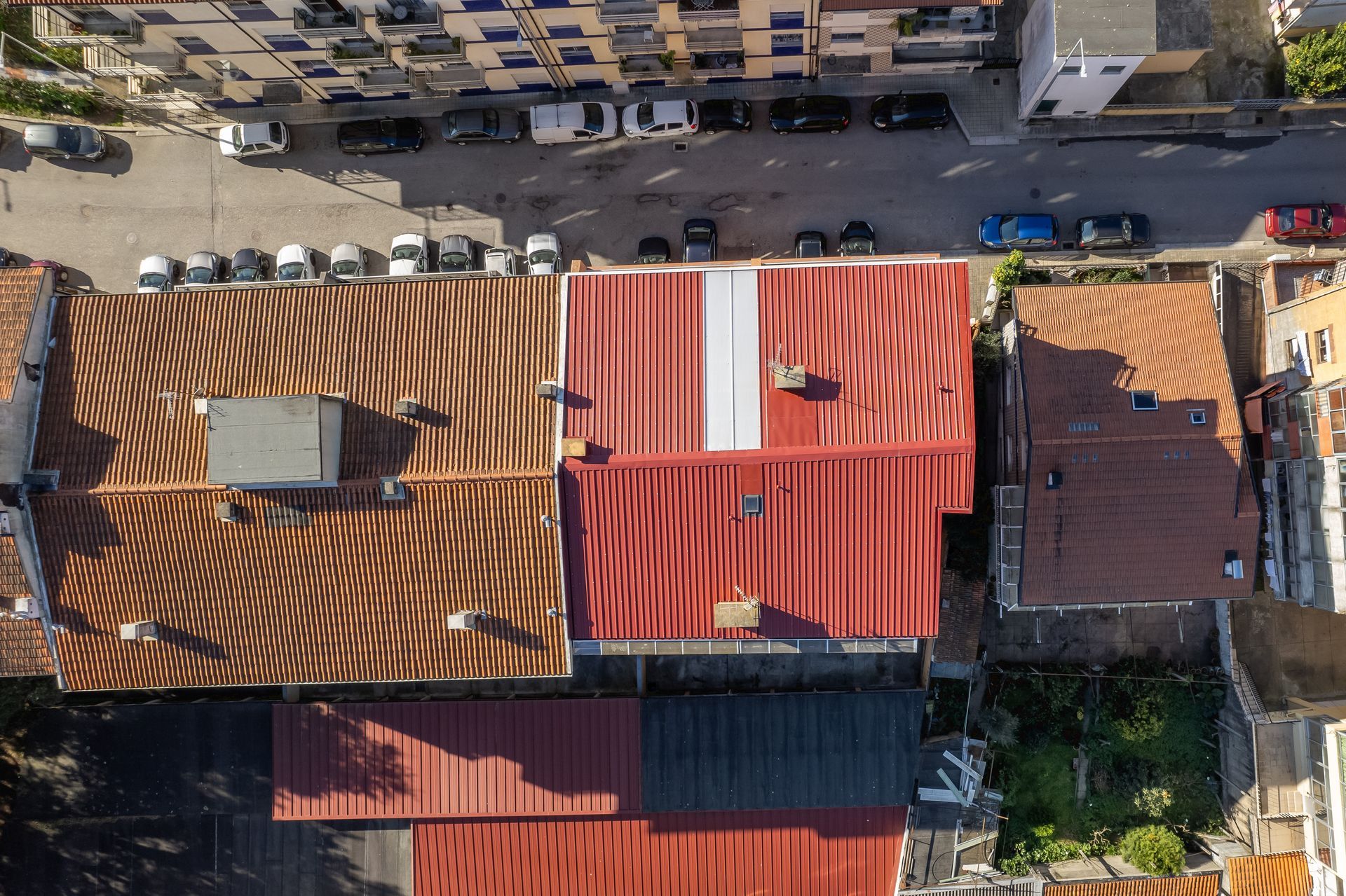 Vista aérea dos telhados de uma cidade. Telhados vermelhos, marrons e cinzas. Carros estacionados na rua.