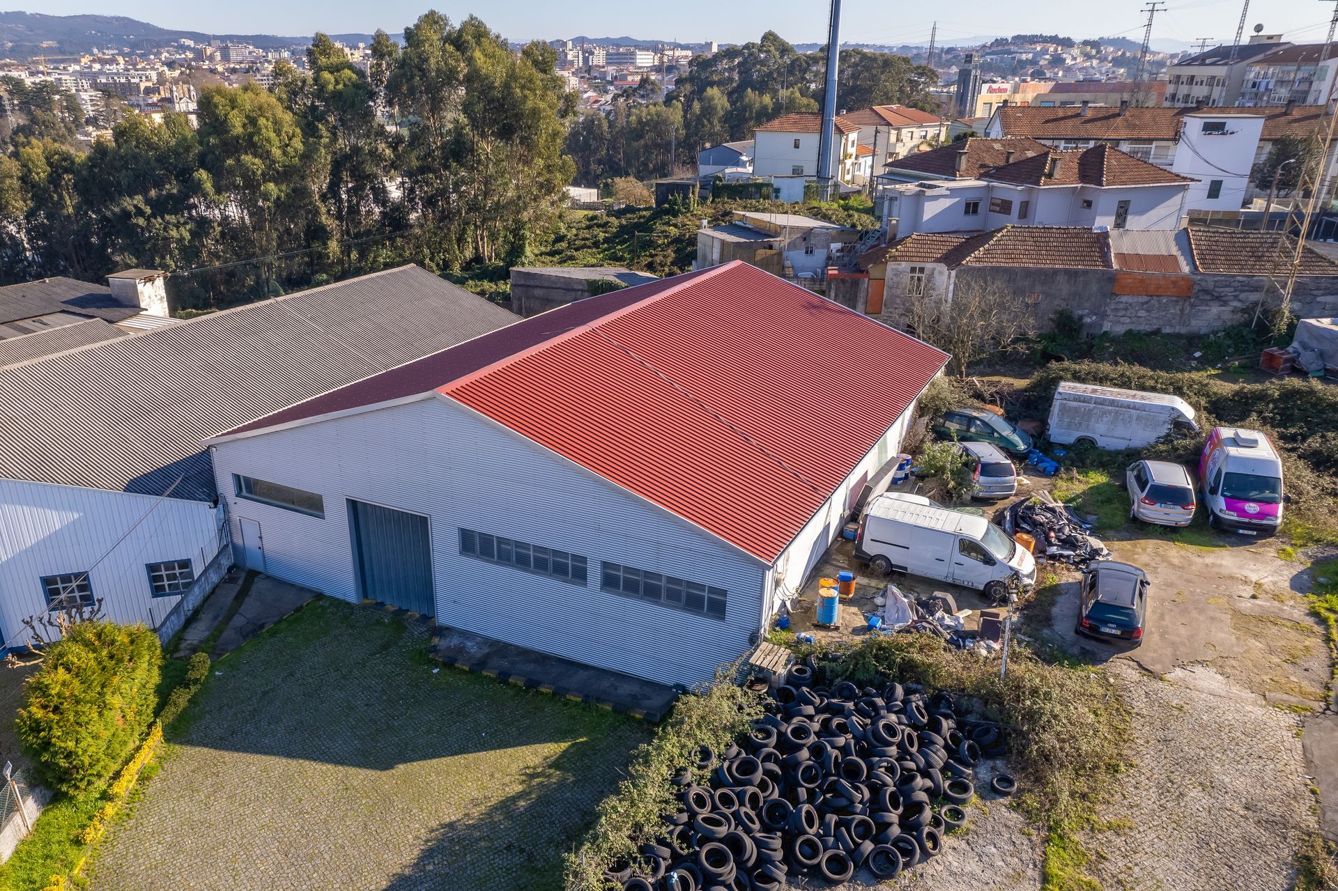 Vista aérea de edifícios industriais com telhado vermelho, pneus e veículos estacionados em um ambiente urbano.