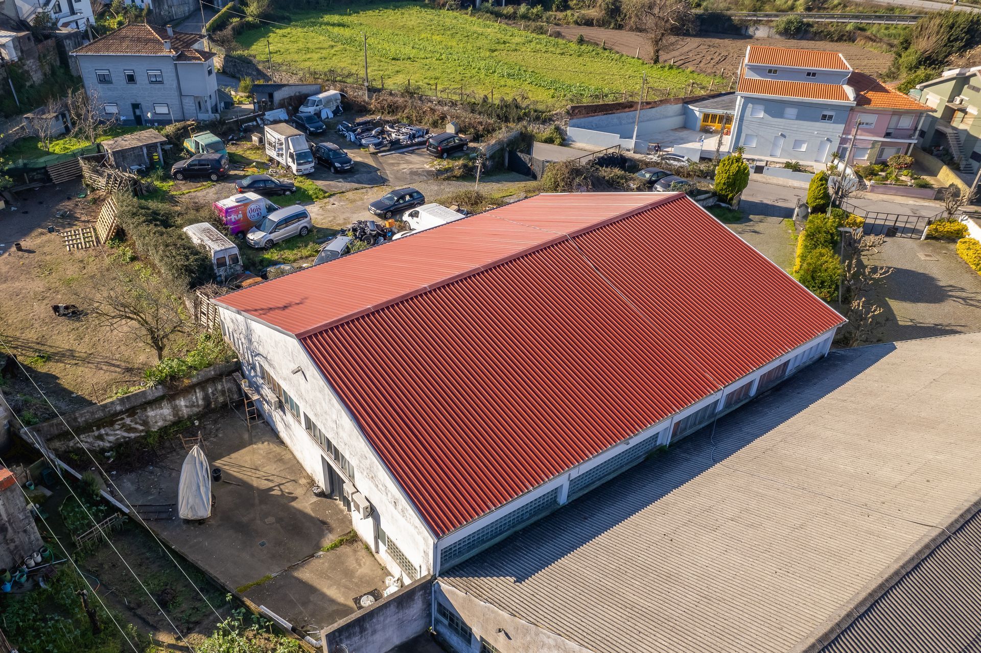 Vista aérea de um edifício com telhado de zinco vermelho, cercado por outros edifícios, veículos e vegetação.
