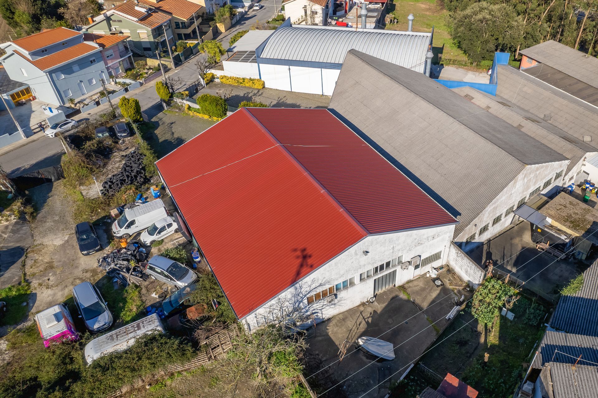 Vista aérea de edifícios industriais com telhados vermelhos e cinzentos, rodeados por veículos estacionados.