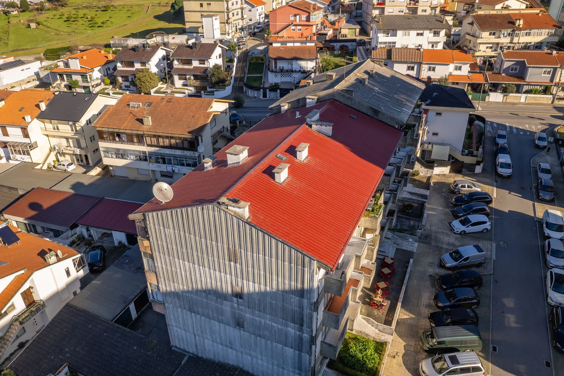 Vista aérea de edifícios com telhados de telha vermelha e carros estacionados na rua.