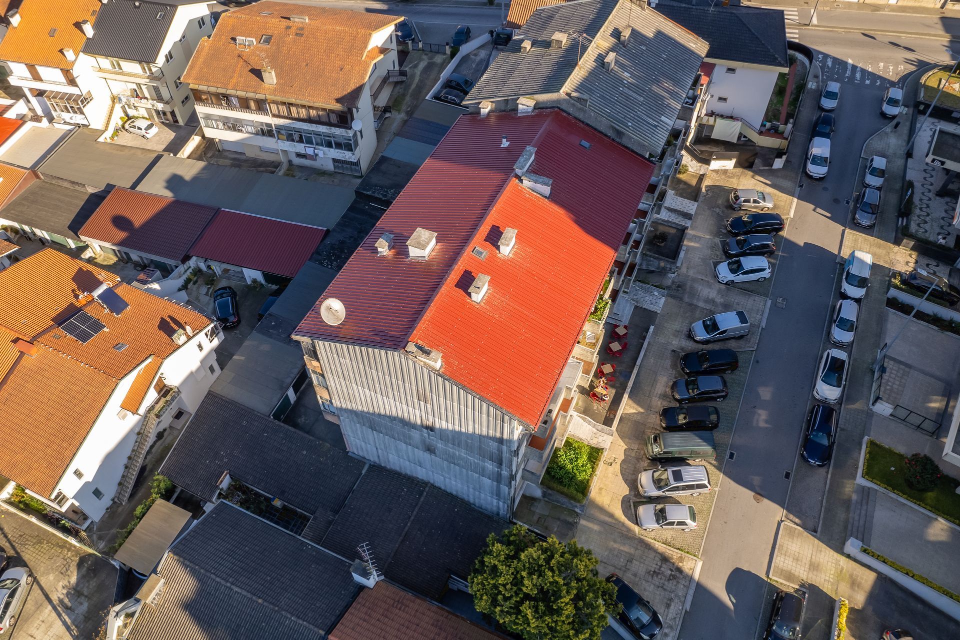 Vista aérea de prédios com telhados vermelhos e marrons, e carros estacionados na rua.