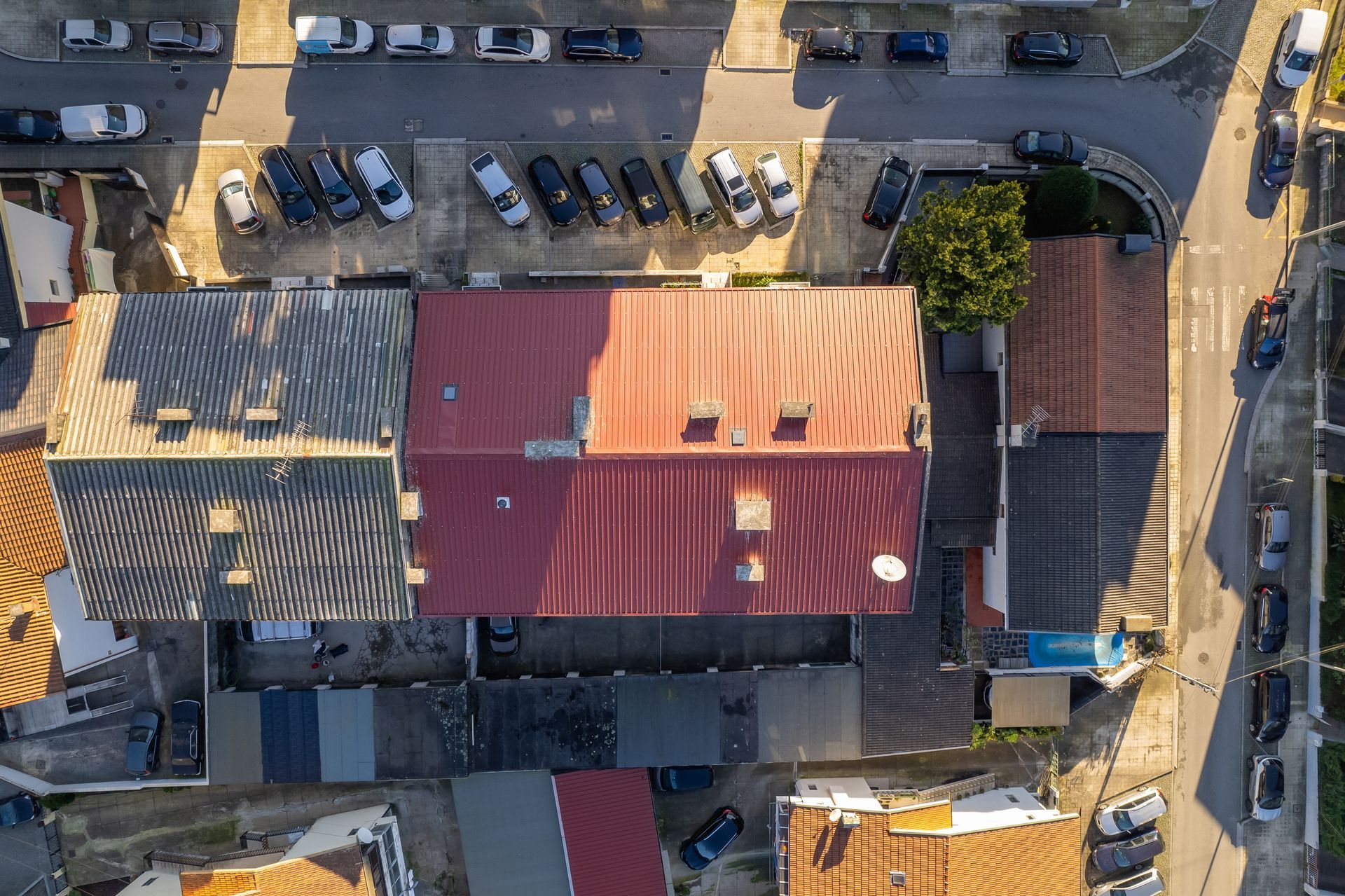 Vista aérea de edifícios com telhados vermelhos e cinzentos, rodeados por carros estacionados e ruas.