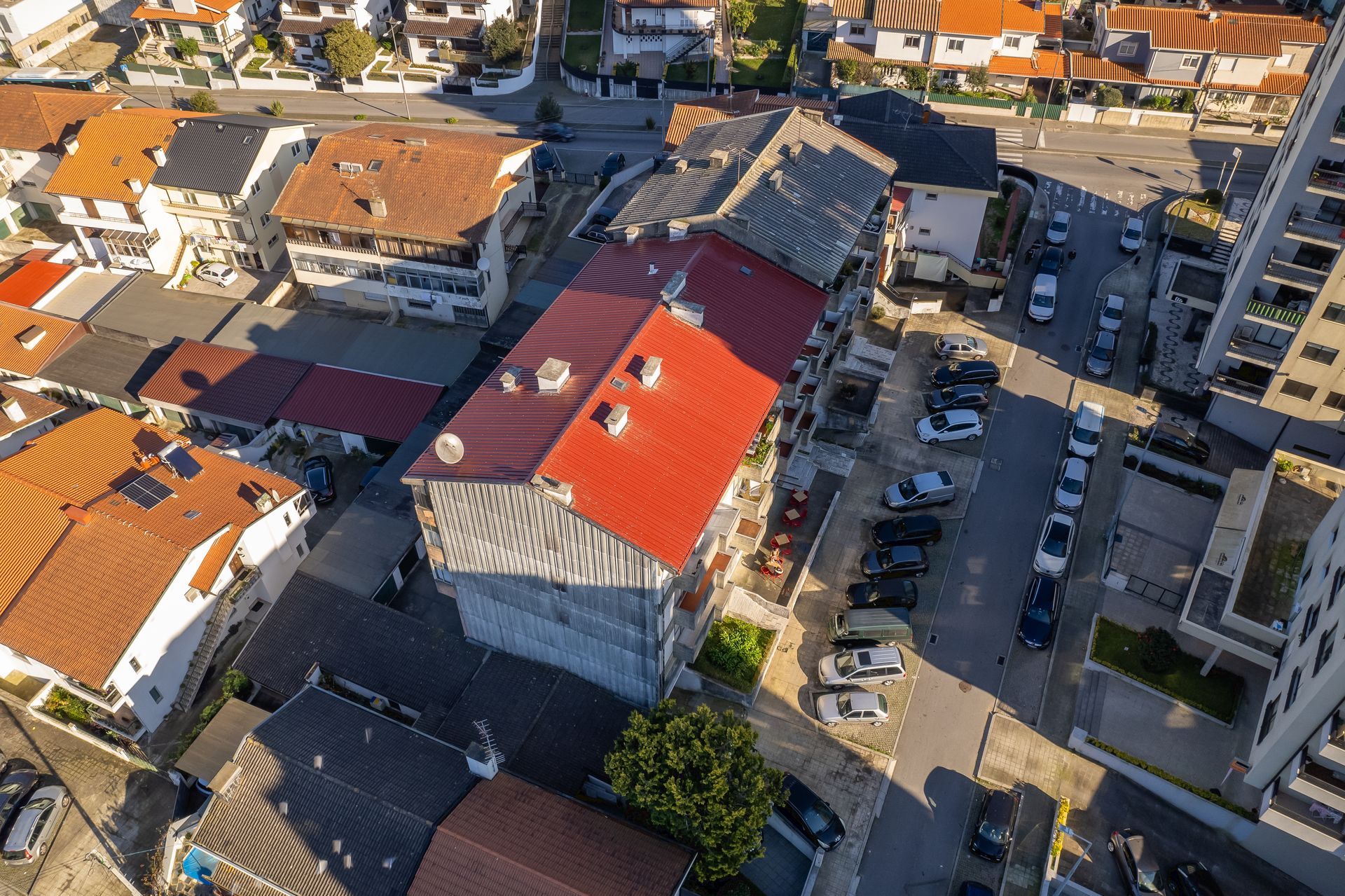 Vista aérea de uma rua da cidade com prédios e carros estacionados. Telhados vermelhos e marrons são predominantes.