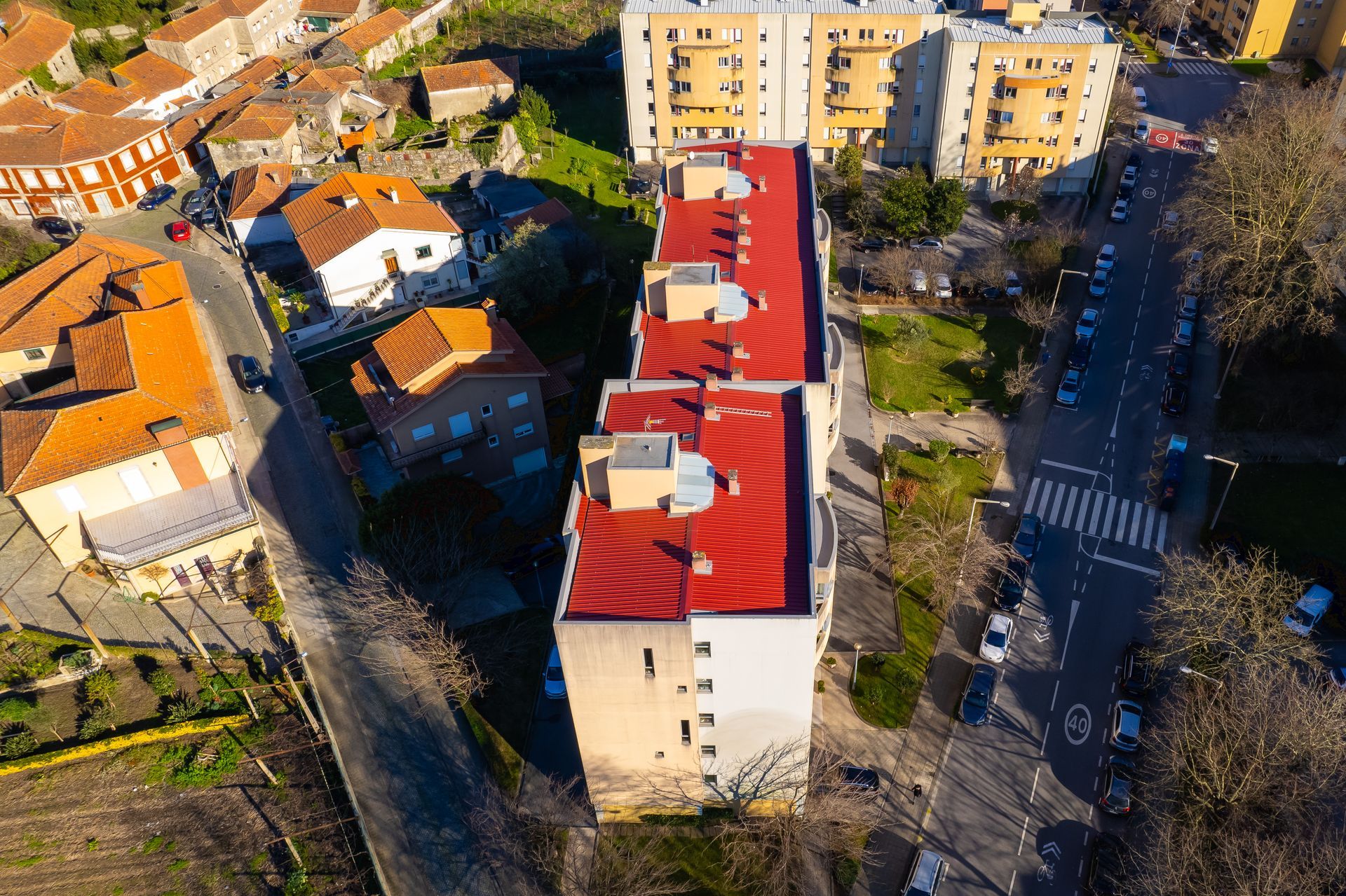 Vista aérea de edifícios com telhados vermelhos, uma estrada e áreas verdes circundantes.