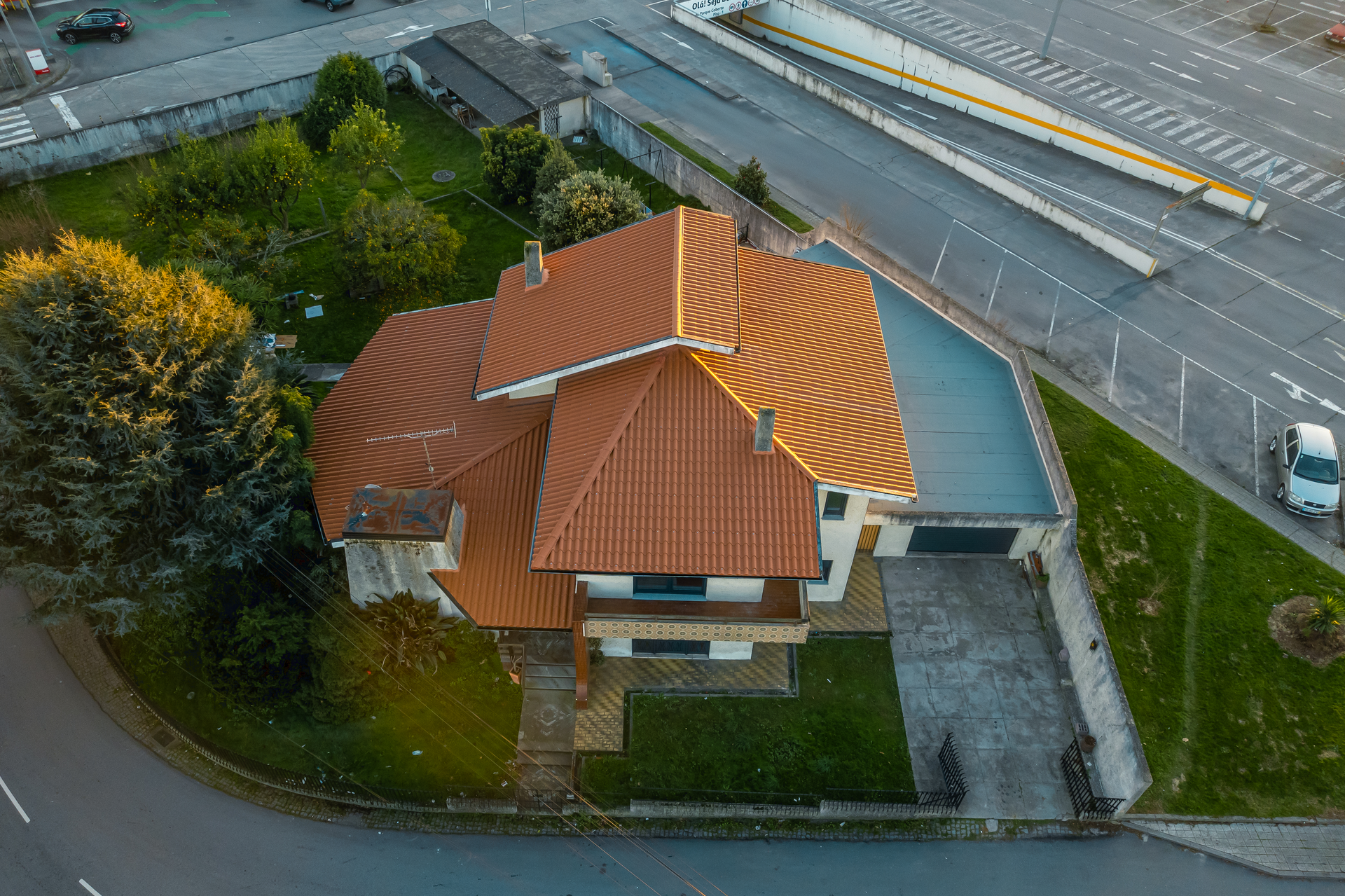 Vista aérea de uma casa com telhado de telhas laranja, ao lado de uma estrada e um estacionamento.