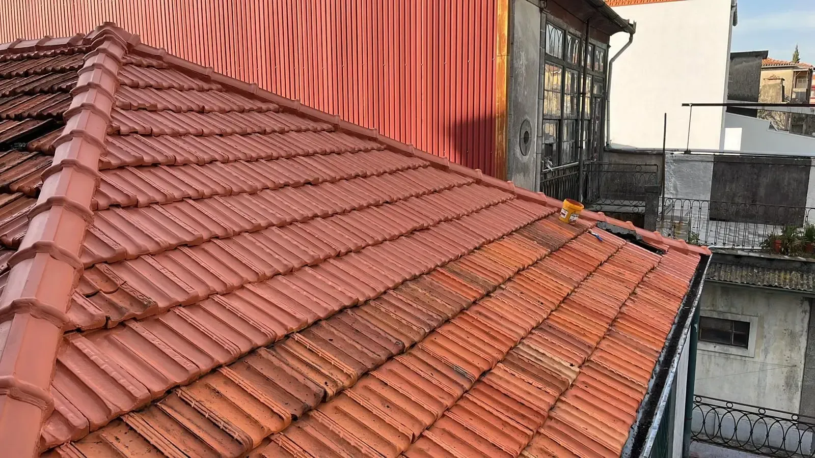 Um close de um telhado de telhas com um prédio vermelho ao fundo.