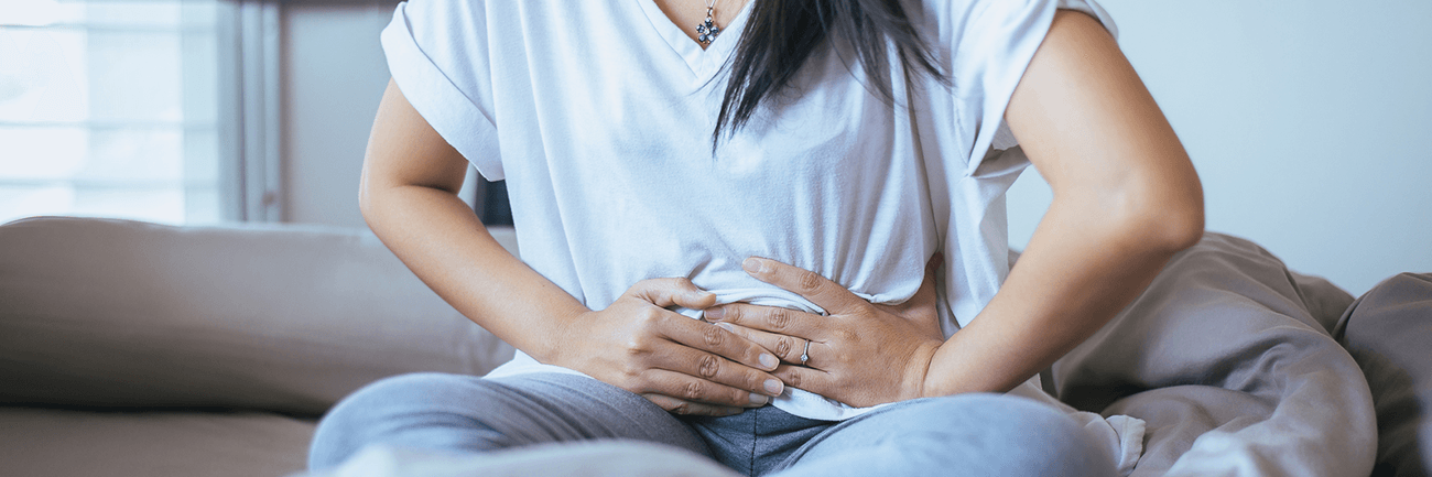 Person seated on a couch clutching their abdomen, suggesting stomach pain or discomfort