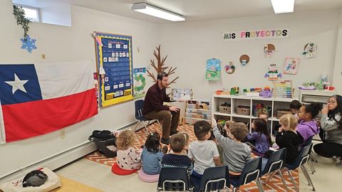 A man is reading a book to a group of children in a classroom.