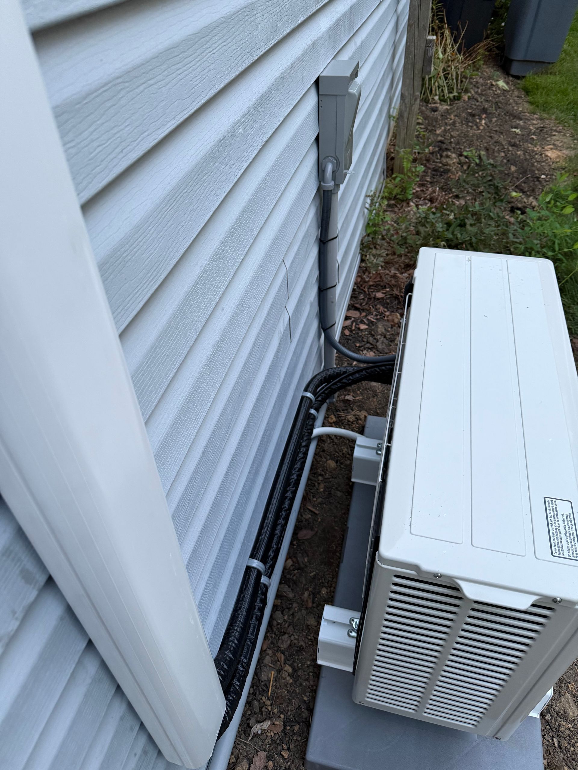 Air conditioner unit attached to the side of a house; black conduit and electrical box are visible.