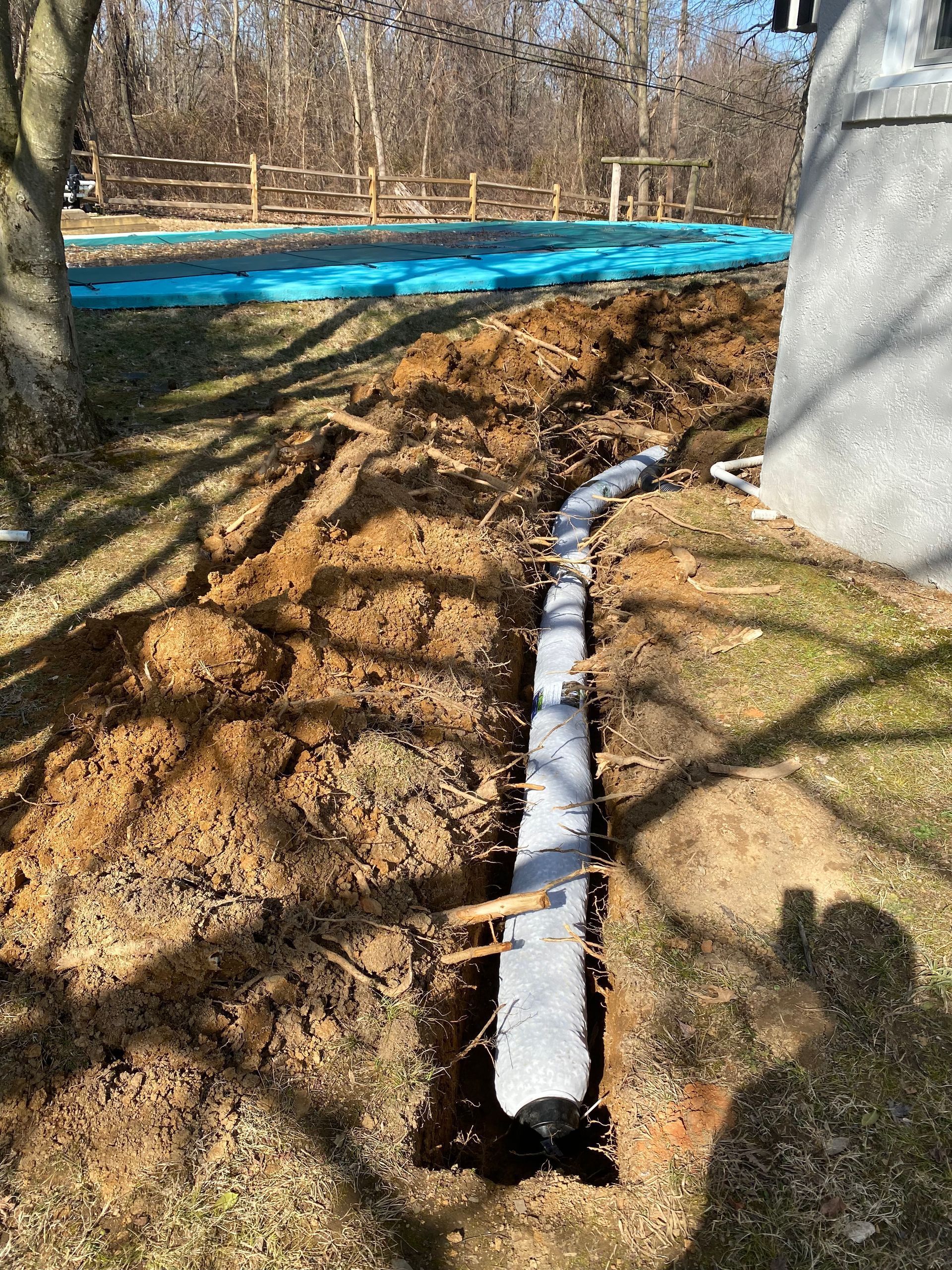A trench with a concrete base near a building is being prepared for drainage.