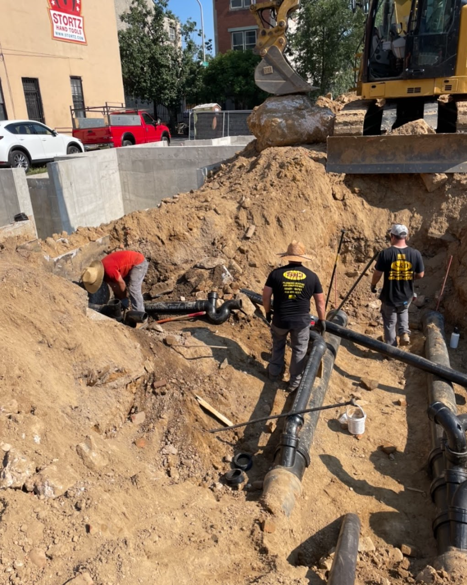 Construction workers installing pipes in an excavated trench. A backhoe is in the background.