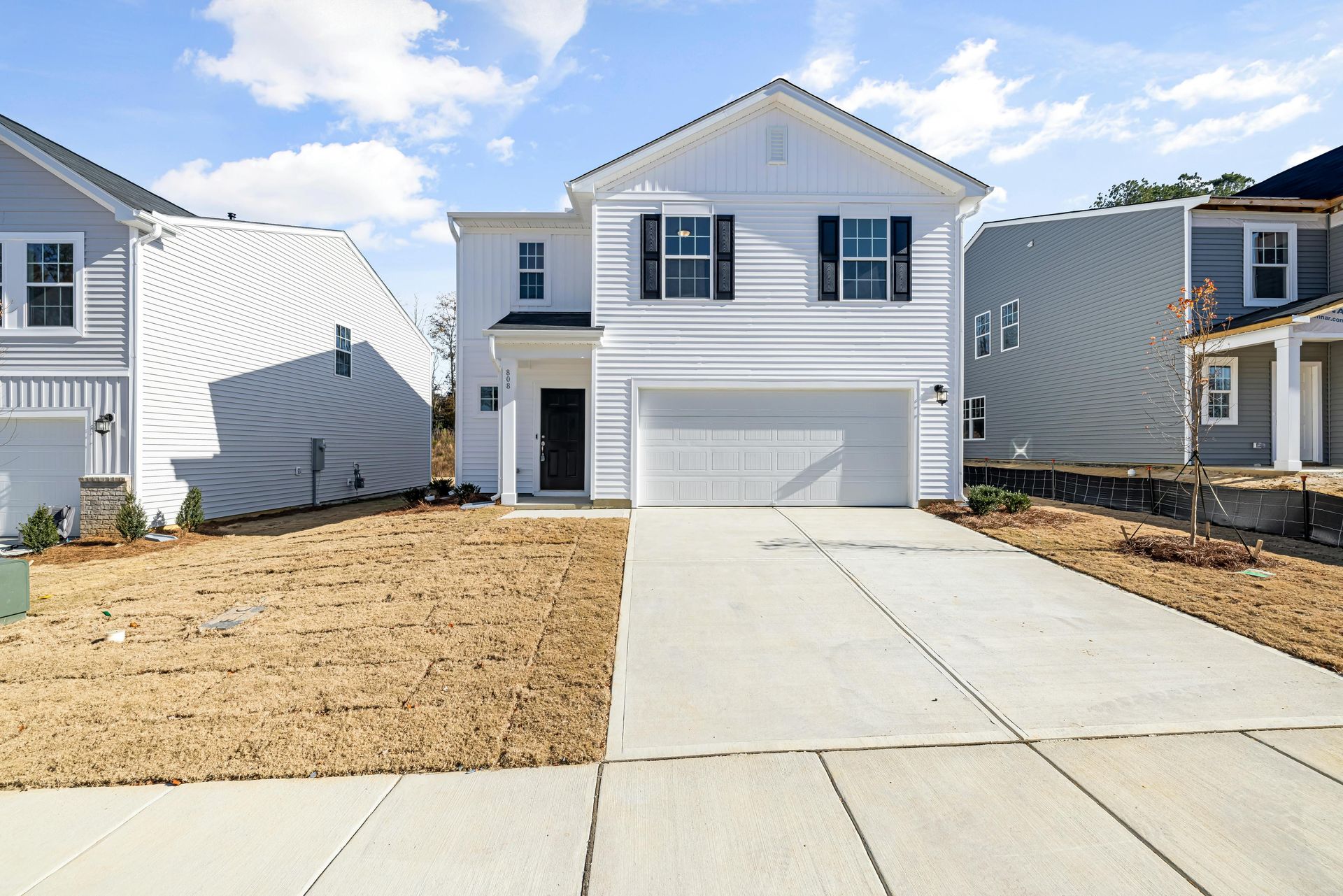 White two-story house with black shutters and attached garage. Concrete driveway, blue sky.