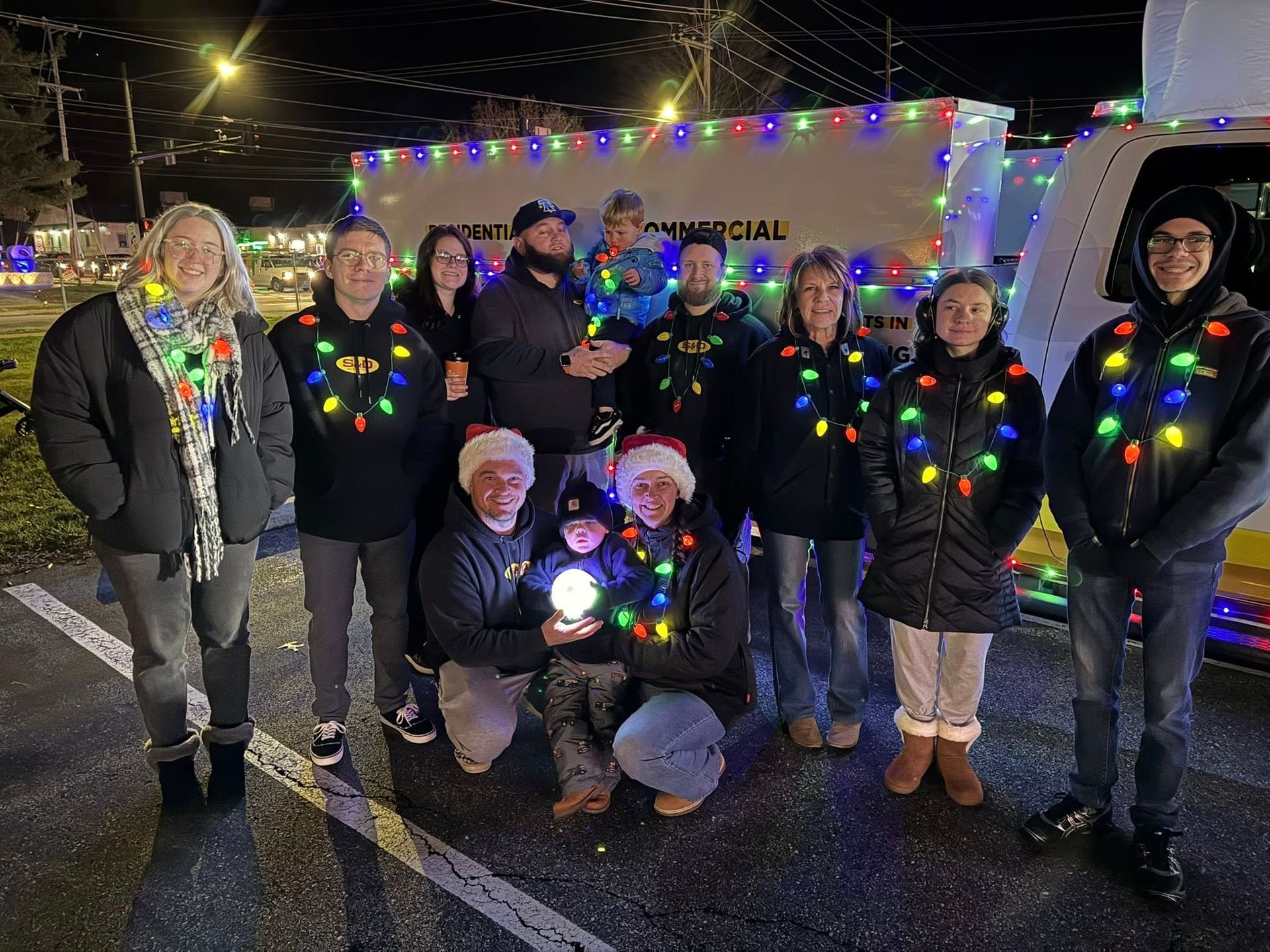 People in black shirts with string lights around necks pose with a decorated float at night.