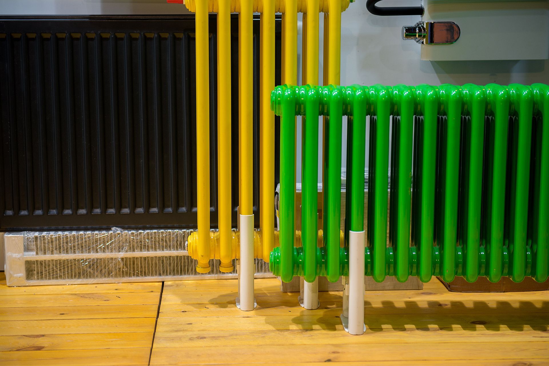 Colorful radiators: black, yellow, and green, set on a wooden floor with white legs.