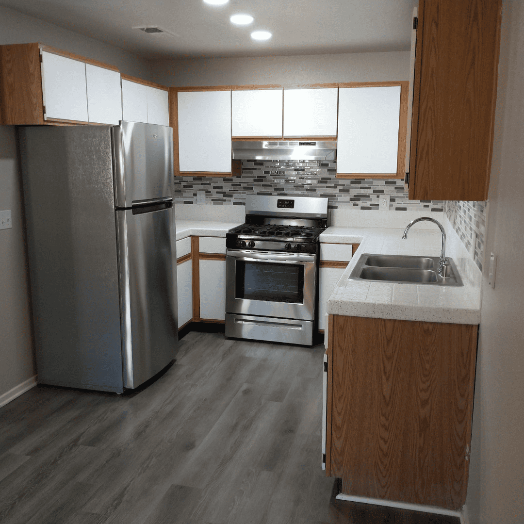 A kitchen with stainless steel appliances and light wood cabinets. White countertops and gray flooring.