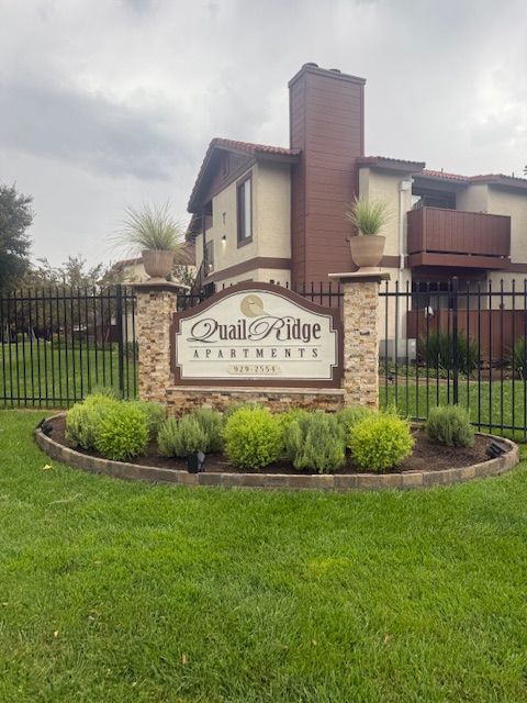 Quail Ridge Apartments sign with brick pillars, landscaped area, and a two-story building in the background.